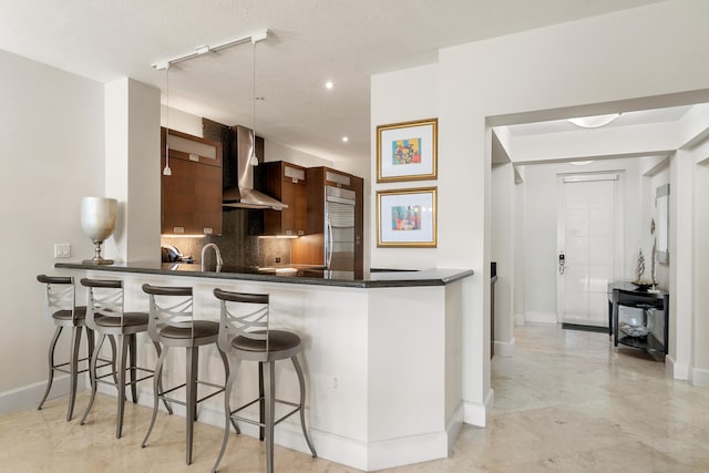 kitchen with tasteful backsplash, kitchen peninsula, wall chimney exhaust hood, and a breakfast bar