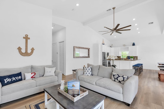 living room with ceiling fan, high vaulted ceiling, beam ceiling, and light hardwood / wood-style floors