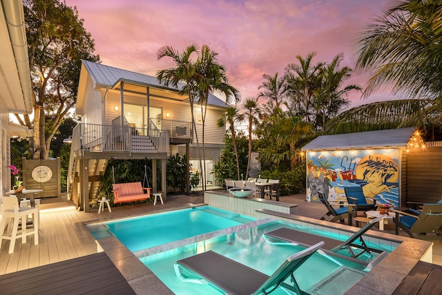 pool at dusk featuring an in ground hot tub and a deck