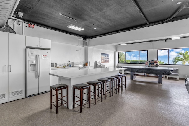 kitchen with white appliances, a breakfast bar, white cabinetry, a center island, and a healthy amount of sunlight