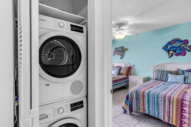 clothes washing area featuring stacked washer / drying machine, ceiling fan, a textured ceiling, and light tile patterned flooring