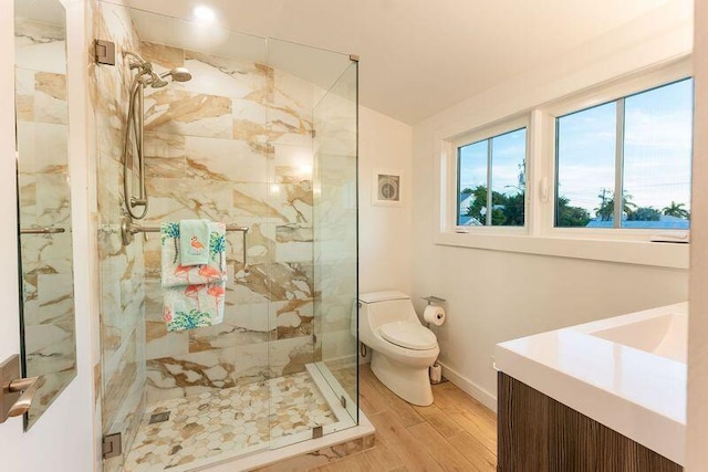 bathroom with a marble finish shower, toilet, wood finished floors, and vanity
