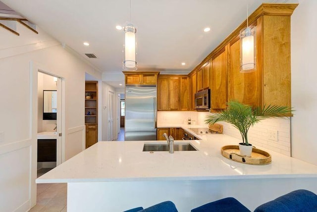 kitchen featuring brown cabinetry, a peninsula, a sink, light countertops, and appliances with stainless steel finishes