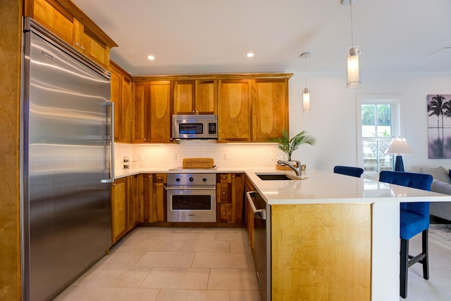 kitchen featuring a breakfast bar, decorative backsplash, appliances with stainless steel finishes, brown cabinetry, and a sink