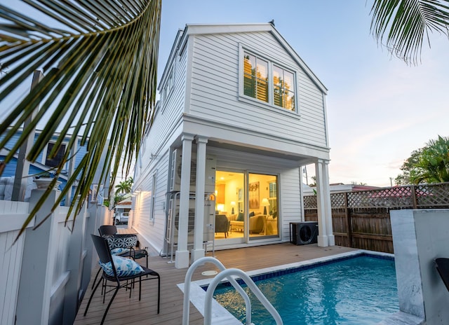 back of property with ac unit, a fenced in pool, a deck, and fence