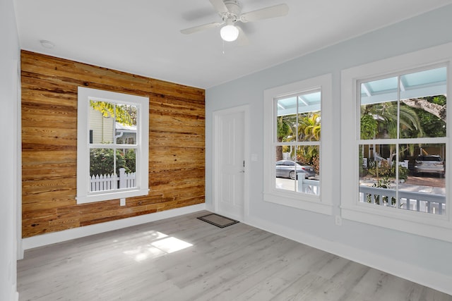 interior space with light hardwood / wood-style flooring, wooden walls, and ceiling fan