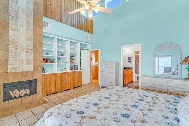 bedroom with connected bathroom, a fireplace, a high ceiling, and light tile patterned floors