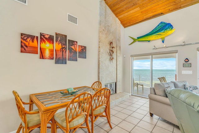 tiled dining area with a water view, wooden ceiling, high vaulted ceiling, and a fireplace