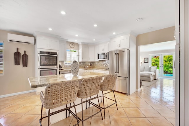 kitchen featuring a breakfast bar, white cabinetry, an AC wall unit, stainless steel appliances, and light stone countertops