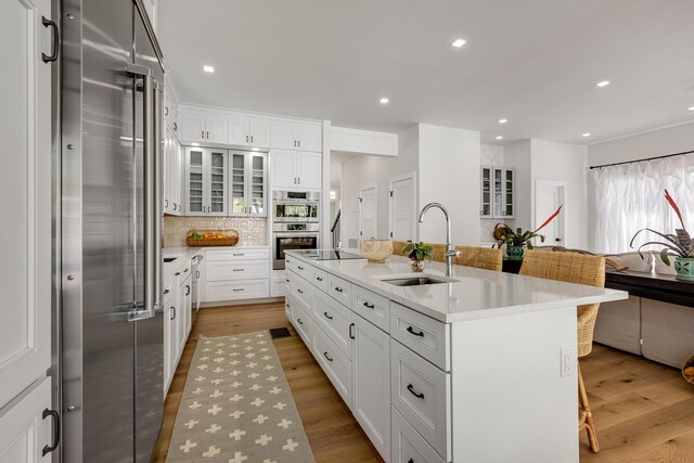 1114 Grinnell St, Key West, FL 33040 - kitchen featuring appliances with stainless steel finishes, a breakfast bar area, white cabinets, a kitchen island with sink, and backsplash