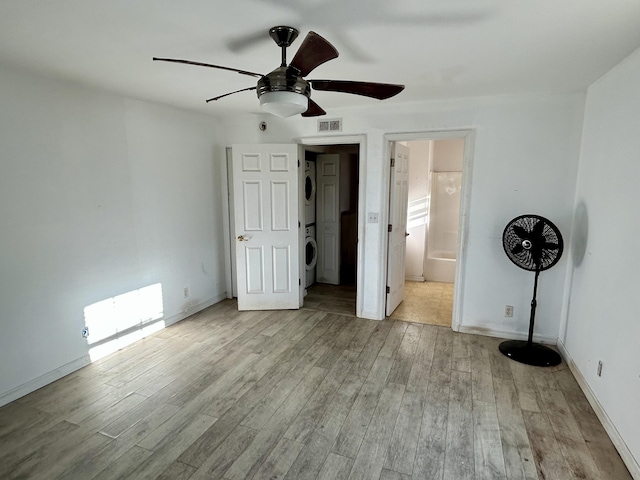 unfurnished bedroom with light wood-type flooring, ceiling fan, and stacked washer / dryer