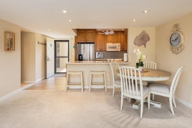 kitchen featuring a kitchen bar, sink, light carpet, stainless steel fridge, and kitchen peninsula