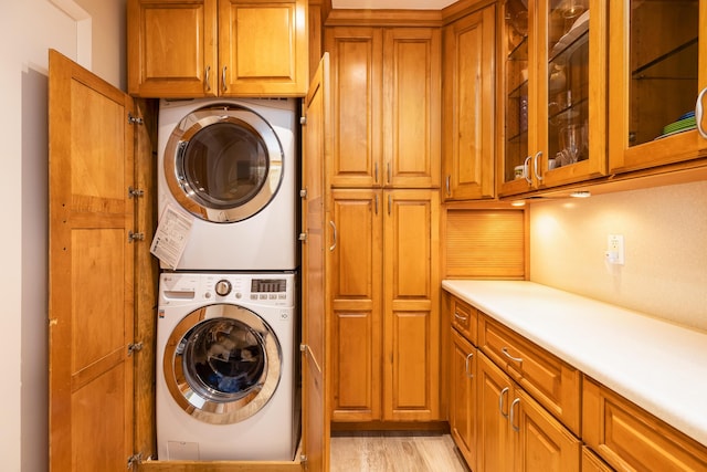 clothes washing area with cabinets, stacked washer and dryer, and light wood-type flooring