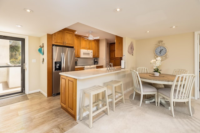 kitchen featuring sink, white appliances, a kitchen breakfast bar, kitchen peninsula, and light wood-type flooring