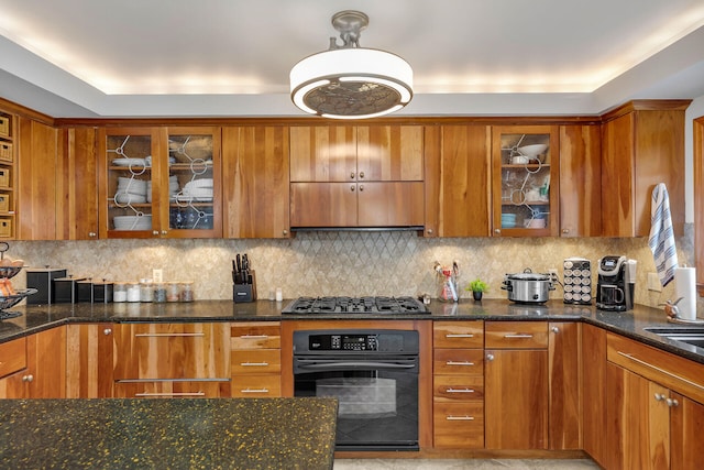 kitchen featuring tasteful backsplash, dark stone counters, brown cabinetry, oven, and stainless steel gas cooktop