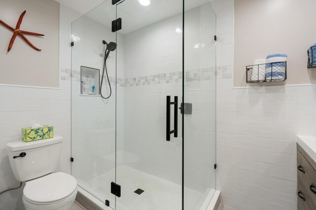 bathroom featuring walk in shower, tile walls, vanity, and toilet