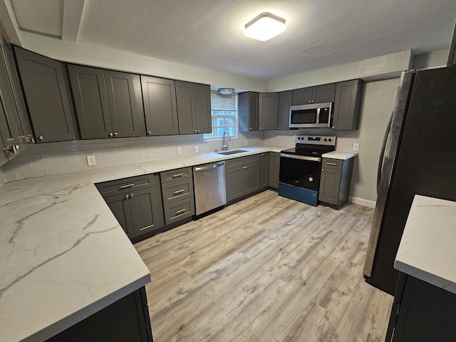 kitchen with sink, stainless steel appliances, light stone counters, tasteful backsplash, and light wood-type flooring