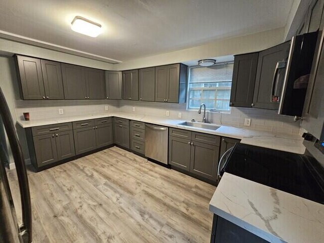 kitchen featuring sink, tasteful backsplash, light hardwood / wood-style flooring, dishwasher, and light stone countertops