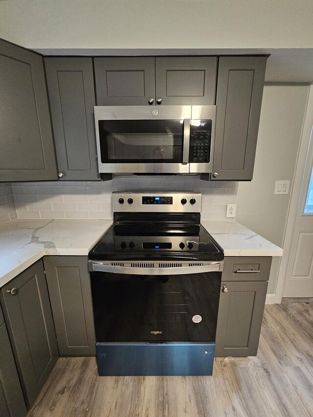 kitchen with light stone countertops, gray cabinets, and stainless steel appliances