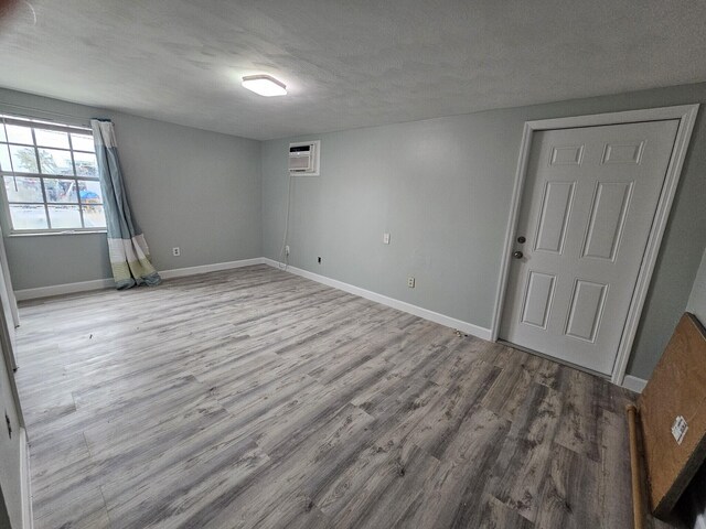 empty room with a textured ceiling, a wall mounted AC, and light wood-type flooring