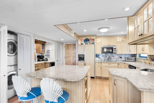 kitchen featuring stacked washing maching and dryer, a center island, backsplash, and a kitchen bar