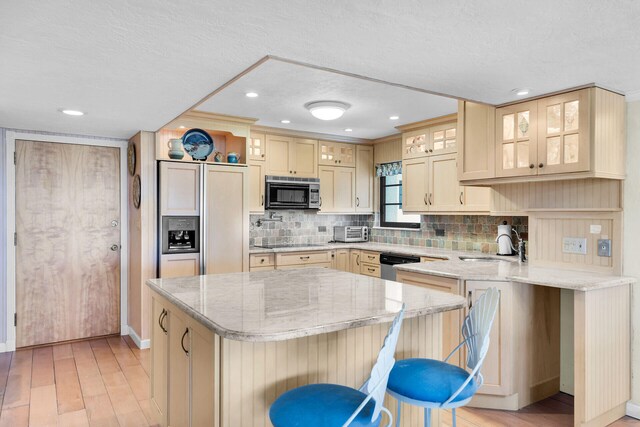 kitchen with a breakfast bar, sink, black electric stovetop, stainless steel dishwasher, and light stone countertops