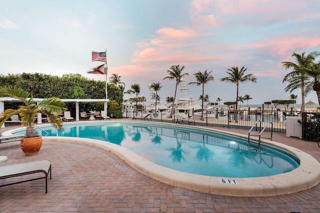 pool at dusk featuring a water view and a patio area