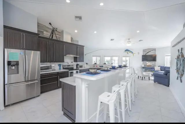 kitchen featuring a center island, dark brown cabinets, appliances with stainless steel finishes, a kitchen breakfast bar, and ceiling fan