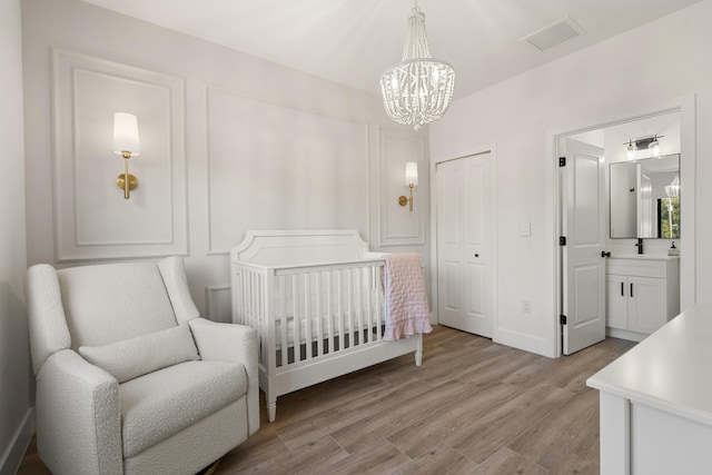 bedroom featuring ensuite bathroom, a nursery area, a chandelier, light hardwood / wood-style floors, and a closet