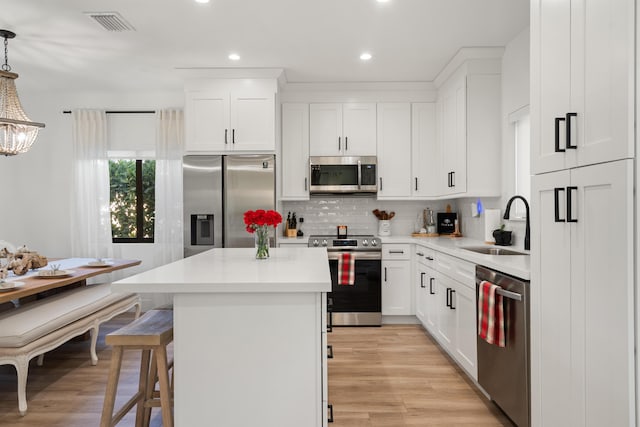 kitchen with white cabinetry, stainless steel appliances, decorative light fixtures, and sink