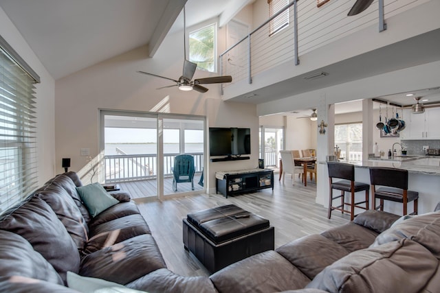 living room with ceiling fan, high vaulted ceiling, sink, and light hardwood / wood-style flooring