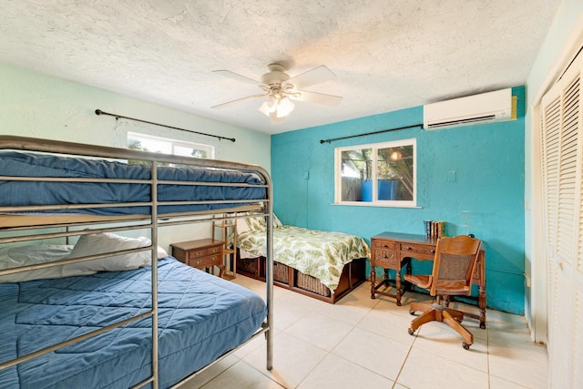 bedroom with an AC wall unit, light tile patterned floors, ceiling fan, a textured ceiling, and a closet