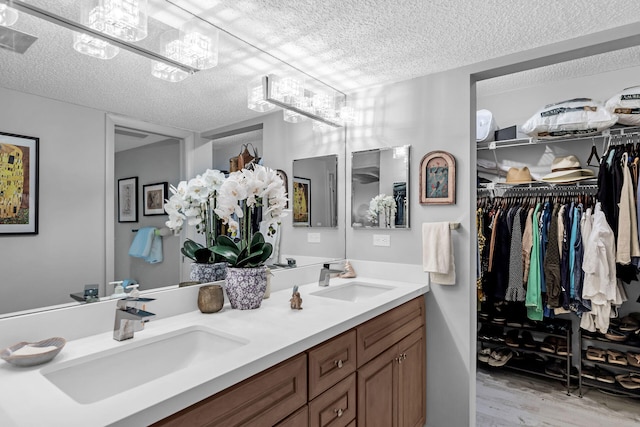 bathroom featuring a textured ceiling, double vanity, a chandelier, and a sink