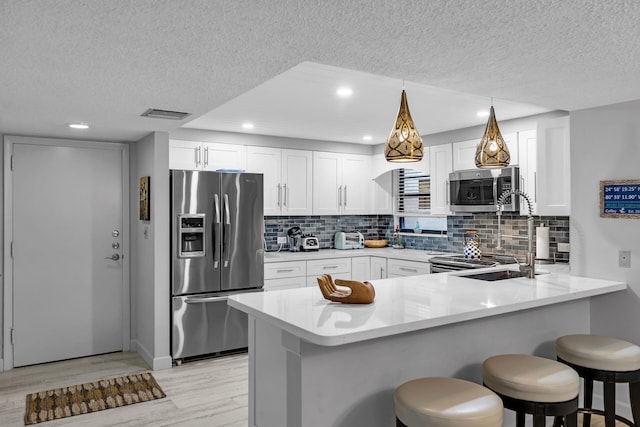 kitchen featuring light wood-style flooring, white cabinetry, stainless steel appliances, a peninsula, and light countertops