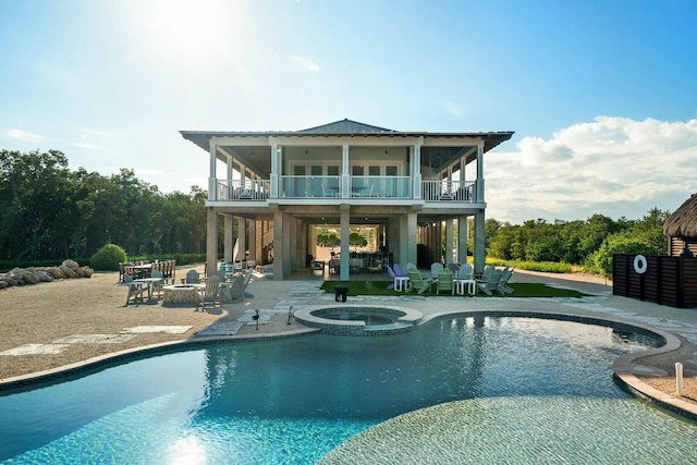 rear view of house featuring a pool with hot tub, a fire pit, a patio, and a balcony