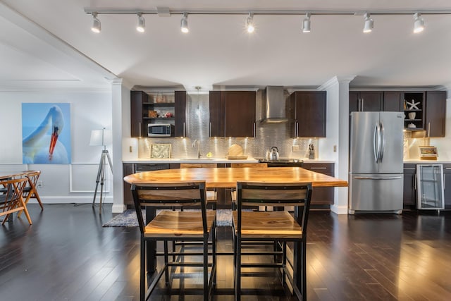 kitchen with appliances with stainless steel finishes, dark hardwood / wood-style floors, dark brown cabinets, and wall chimney range hood