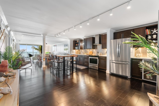 kitchen featuring stainless steel appliances, dark brown cabinets, a kitchen breakfast bar, and wall chimney exhaust hood