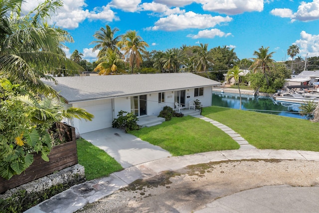 ranch-style house with a water view, stucco siding, a front lawn, an attached garage, and driveway