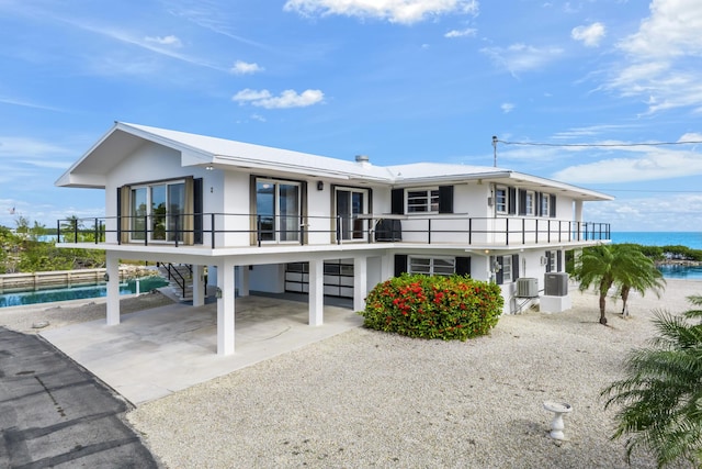 rear view of house with a carport, a balcony, a water view, and central air condition unit