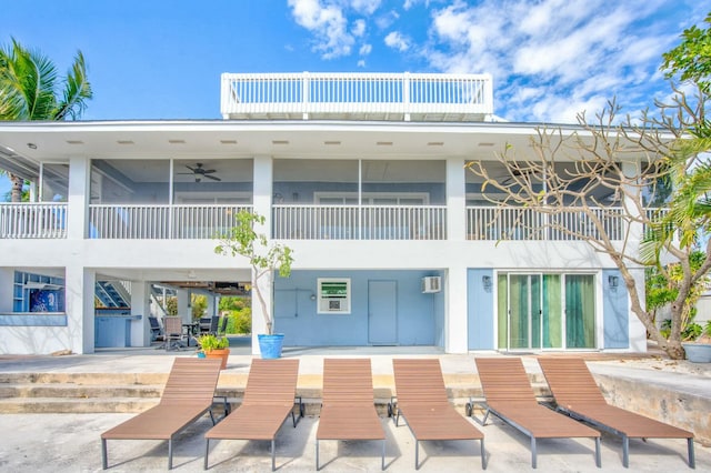 rear view of property featuring a balcony, an AC wall unit, ceiling fan, and a patio area