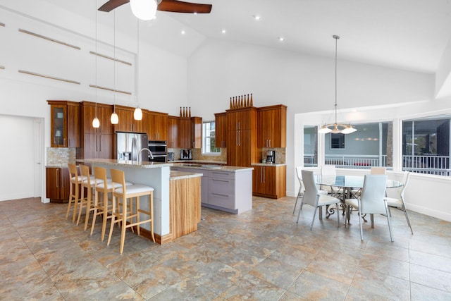 kitchen featuring pendant lighting, an island with sink, a breakfast bar area, stainless steel fridge, and light stone counters