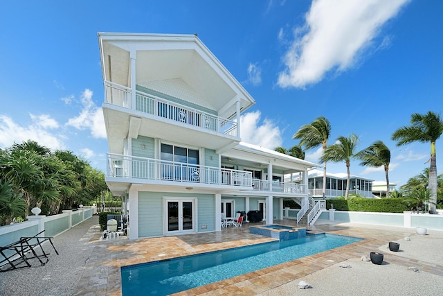 back of house with french doors, a balcony, a swimming pool with hot tub, and a patio