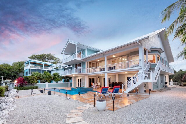 back house at dusk featuring a balcony, a fenced in pool, and a patio