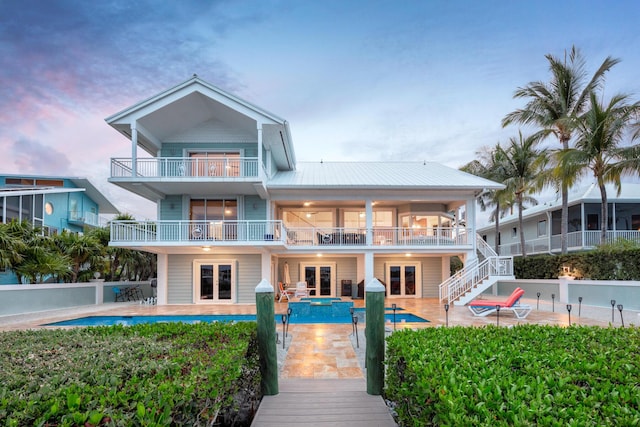 back house at dusk featuring a patio, a balcony, and french doors