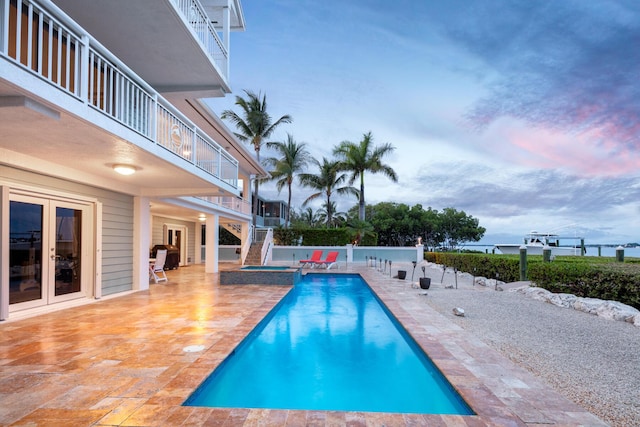 pool at dusk with a patio, an in ground hot tub, and french doors