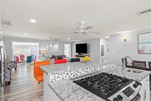 kitchen with a breakfast bar, sink, white cabinetry, light hardwood / wood-style flooring, and light stone countertops