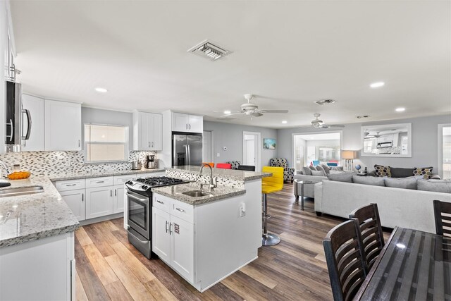 kitchen with sink, appliances with stainless steel finishes, white cabinetry, a kitchen island with sink, and light stone counters