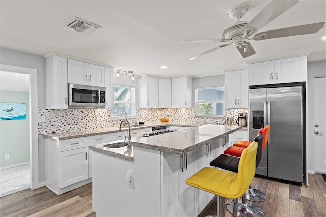 kitchen featuring white cabinetry, light stone countertops, stainless steel appliances, and an island with sink