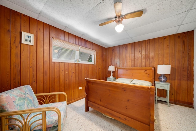 bedroom featuring wooden walls, a drop ceiling, and ceiling fan