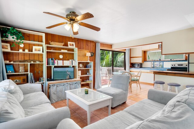 living room featuring ceiling fan, wooden walls, and light tile patterned floors